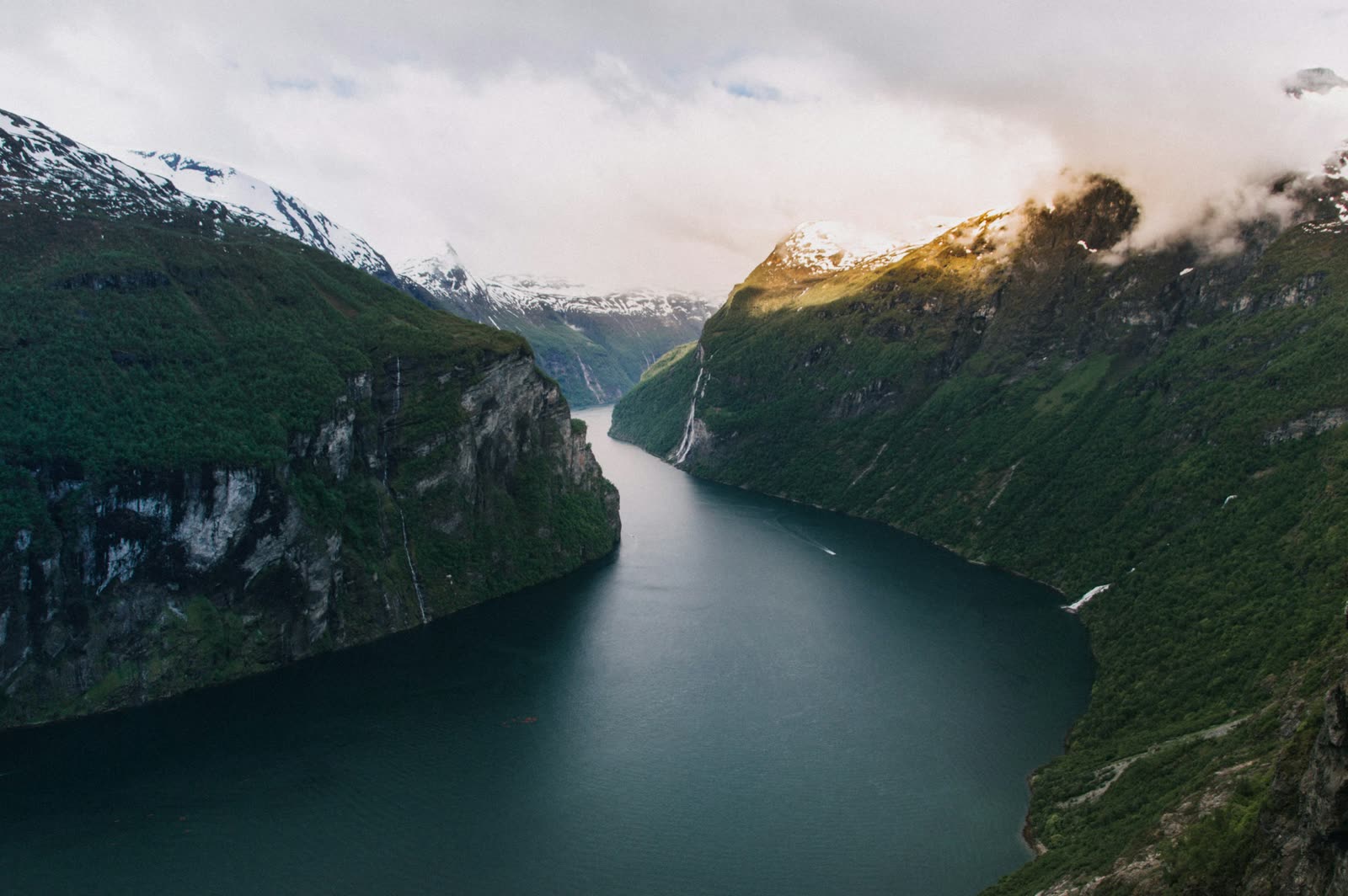 A still fjord reflecting steep mountains under a soft sky