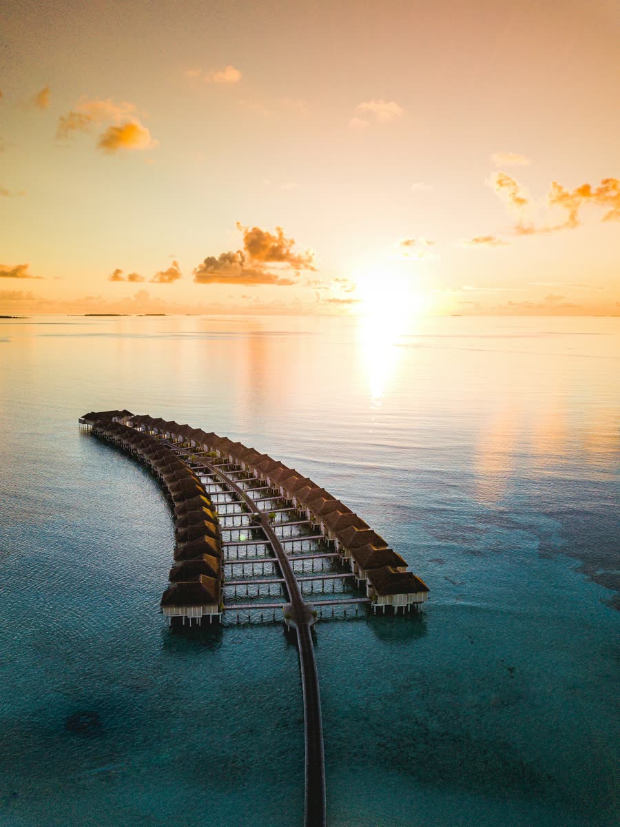 A wooden jetty stretching over calm water at sunset in the Maldives