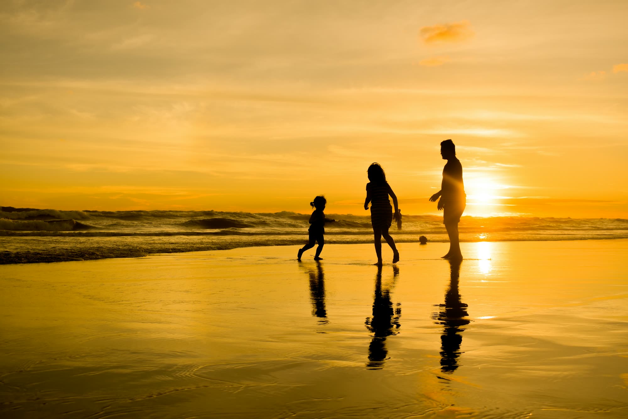 A family playing on a beach at golden sunset, silhouetted against the sea